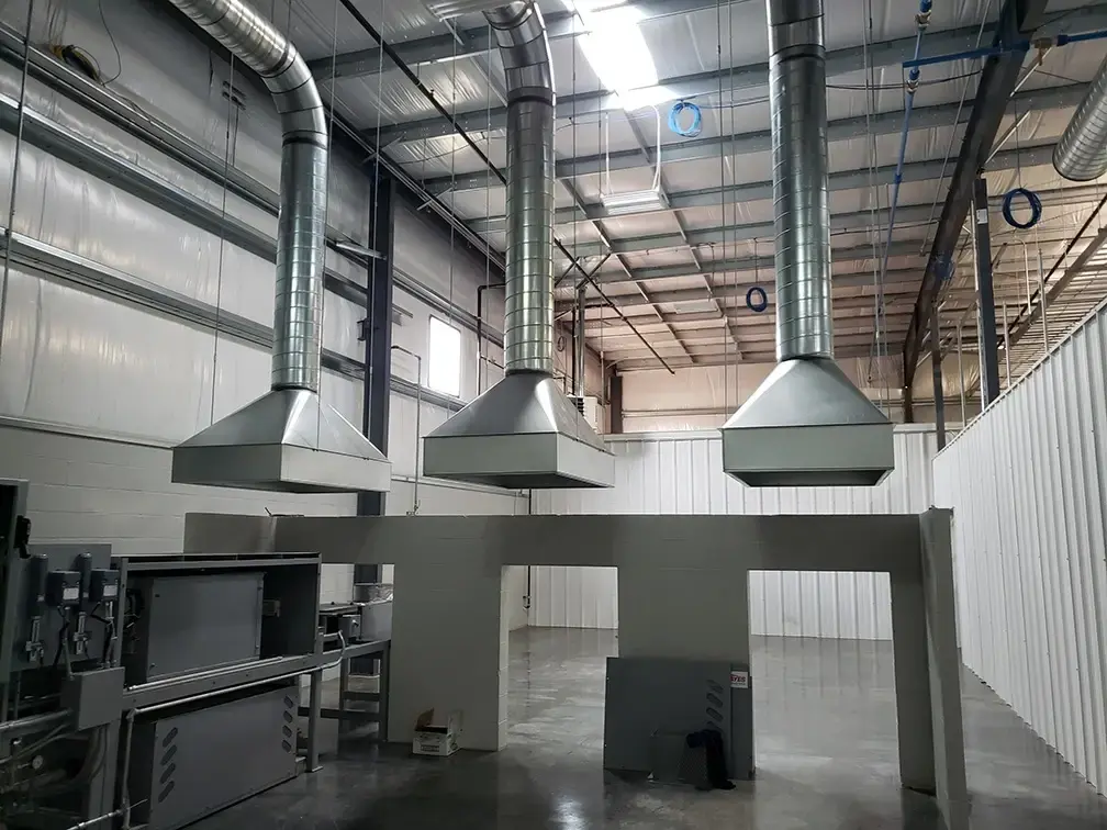 Industrial facility with large metal ventilation hoods and ductwork suspended from the ceiling