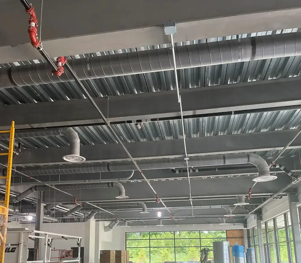 Exposed ceiling with metal ductwork and sprinkler system in an industrial space with large windows