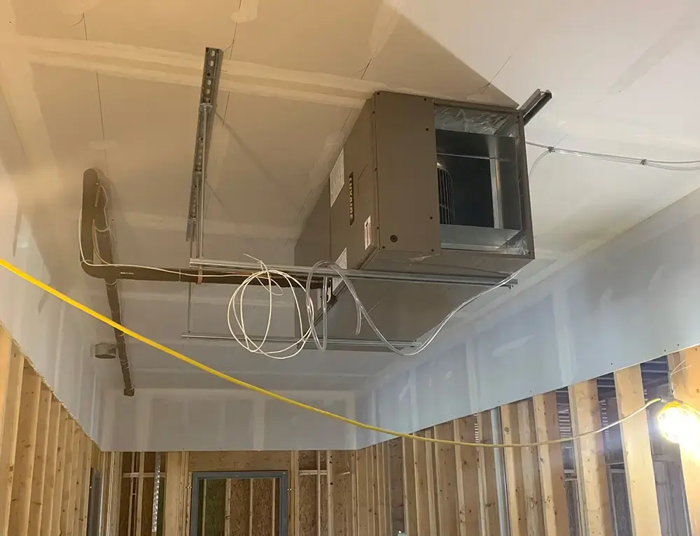 Partially constructed interior with an HVAC unit installed in the ceiling framework and visible wiring