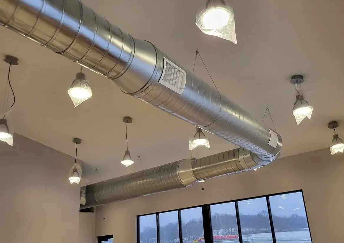 Interior view of a room with exposed metal ductwork and pendant lighting fixtures on the ceiling