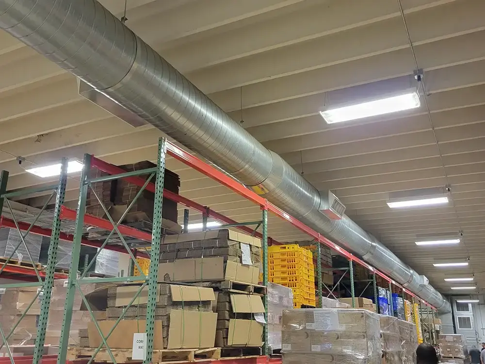 Warehouse interior with metal ductwork running along the ceiling and storage racks filled with boxes