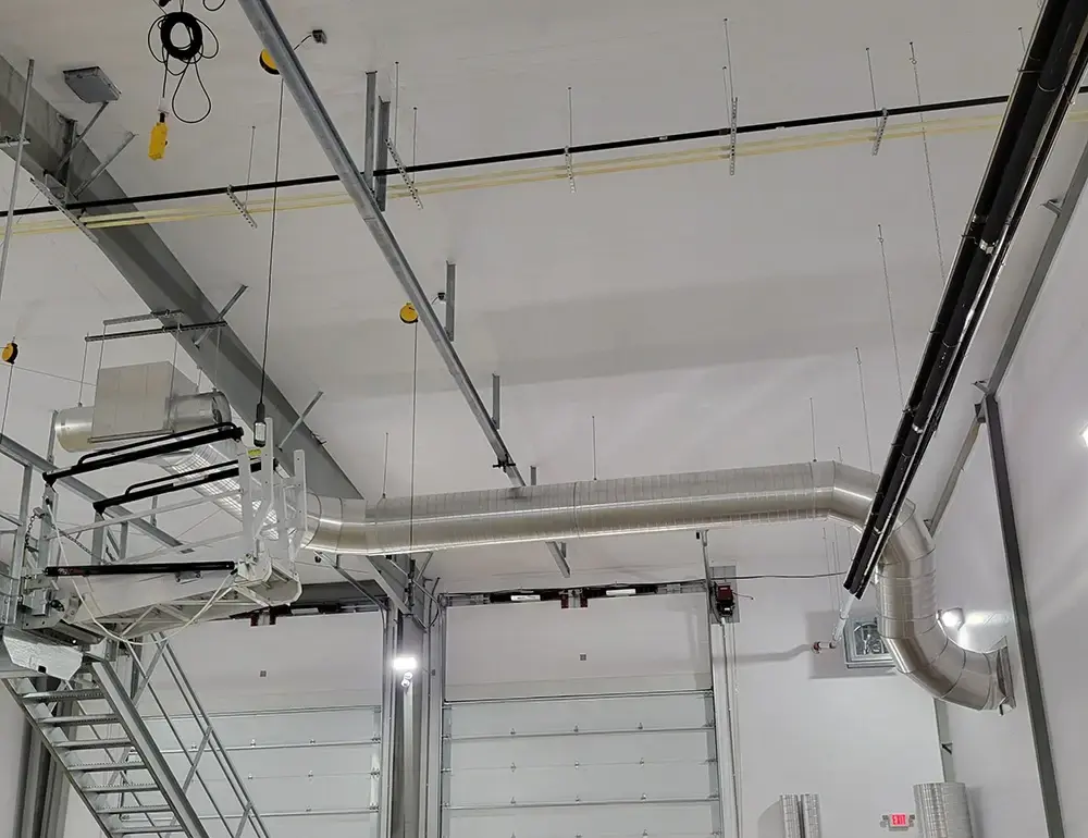 Interior of an industrial facility with exposed ductwork and a metal staircase under a high ceiling