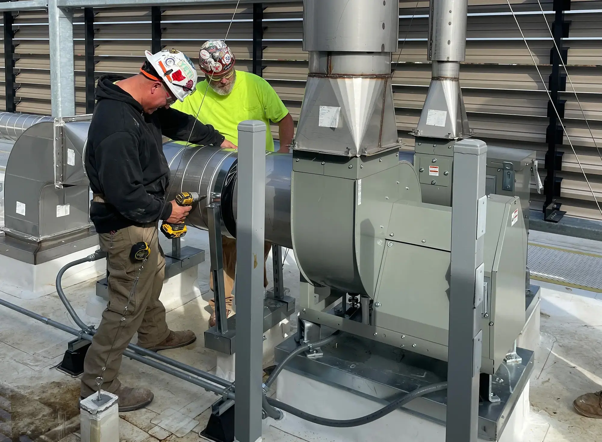 Two YORK workers in hard hats and safety gear are installing a large HVAC unit on a rooftop